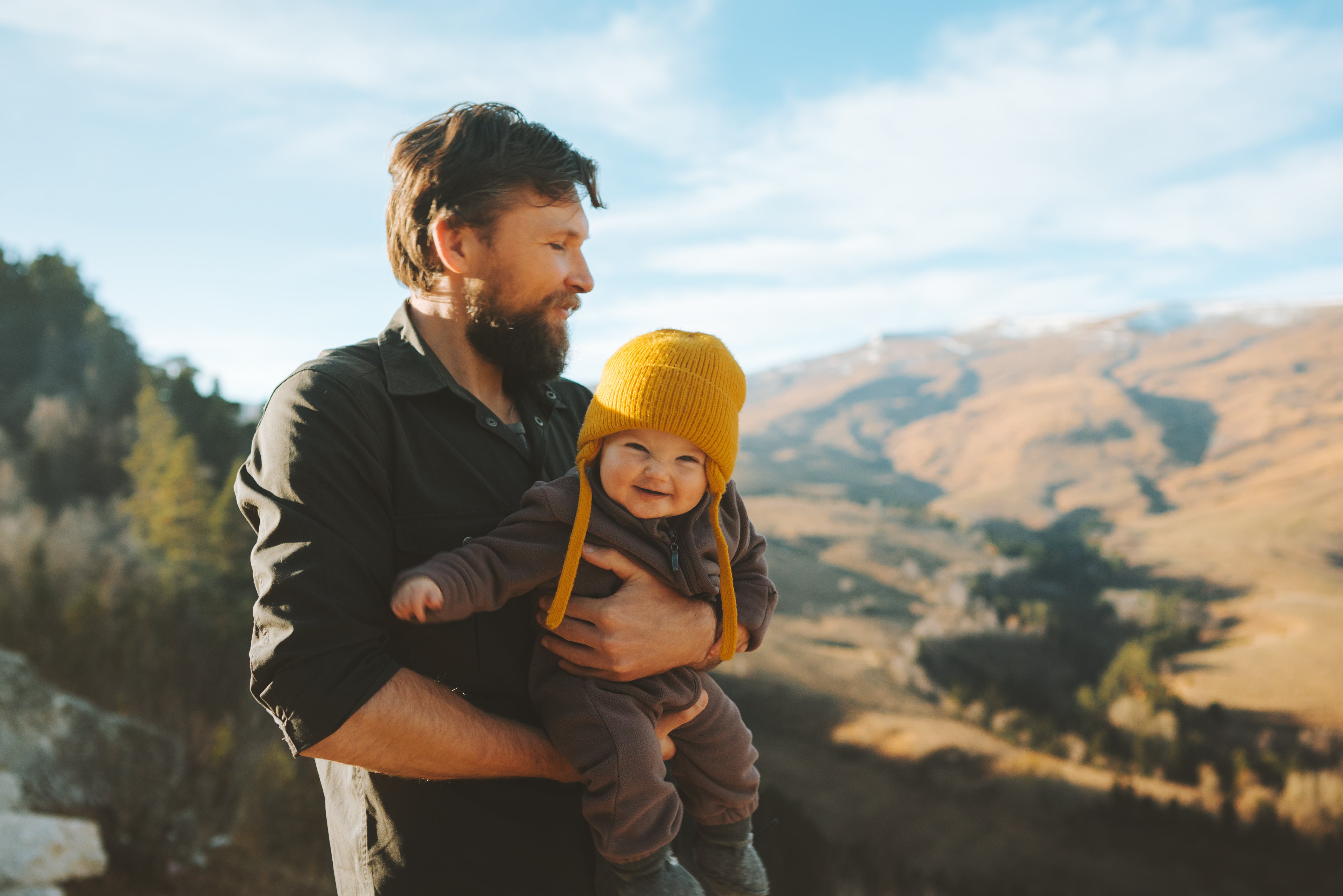 Dad holding an infant baby wearing a hat.