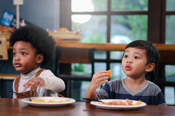 Two toddler boys sitting next to each other sharing a healthy meal.