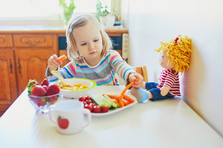 Toddler sitting at the table eating healthy snacks of fruits and vegetables.