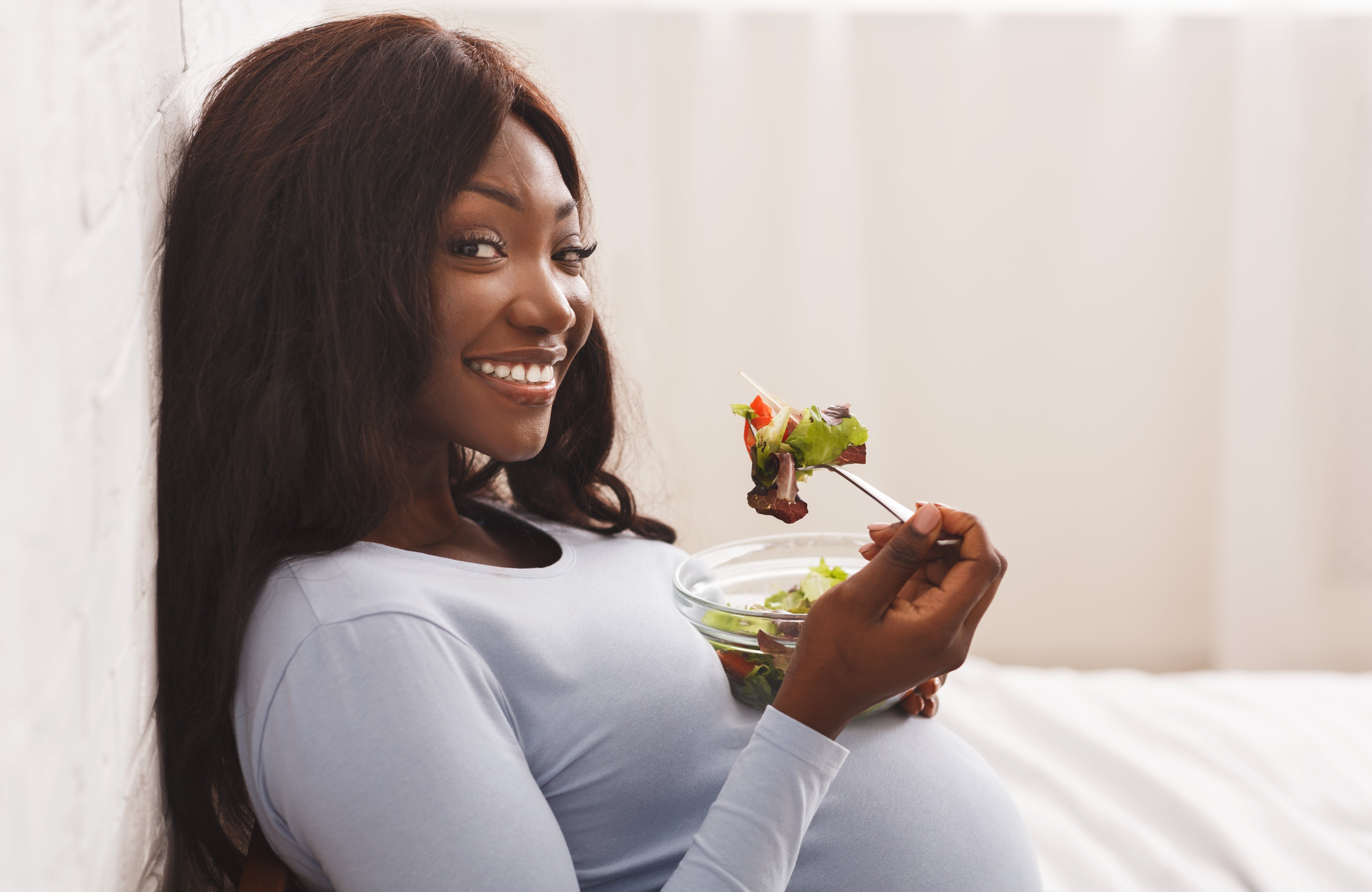 Smiling pregnant woman eating a healthy salad.